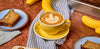 Yellow mug with latte sitting on wood table top with banana bread slices next to it